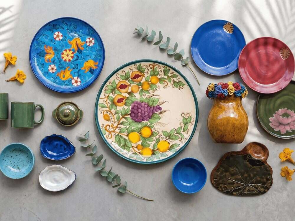 Peças de grés vistas de cima: pratos, canecas e bowls de cores variadas sobre fundo claro