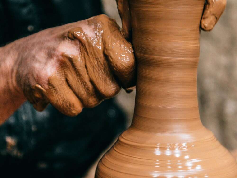 Mãos de ceramista dando forma a um vaso de barro girando no torno