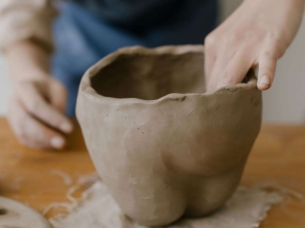 Mãos modelando à mão um bowl de barro cru de borda irregular